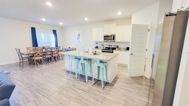 kitchen featuring light hardwood / wood-style flooring, an island with sink, a kitchen bar, white cabinetry, and appliances with stainless steel finishes