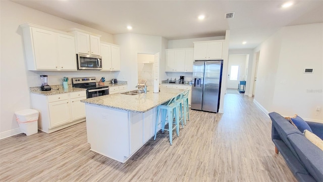 kitchen featuring light hardwood / wood-style floors, stainless steel appliances, an island with sink, white cabinets, and a kitchen bar