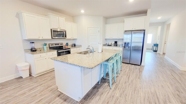 kitchen with stainless steel appliances, sink, white cabinetry, and an island with sink