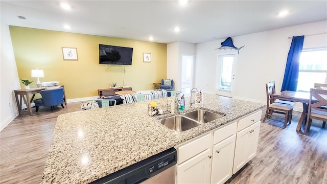 kitchen with light hardwood / wood-style floors, light stone countertops, white cabinetry, a kitchen island with sink, and sink