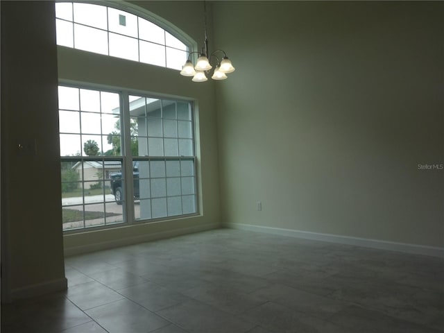 spare room with a healthy amount of sunlight, an inviting chandelier, and dark tile flooring