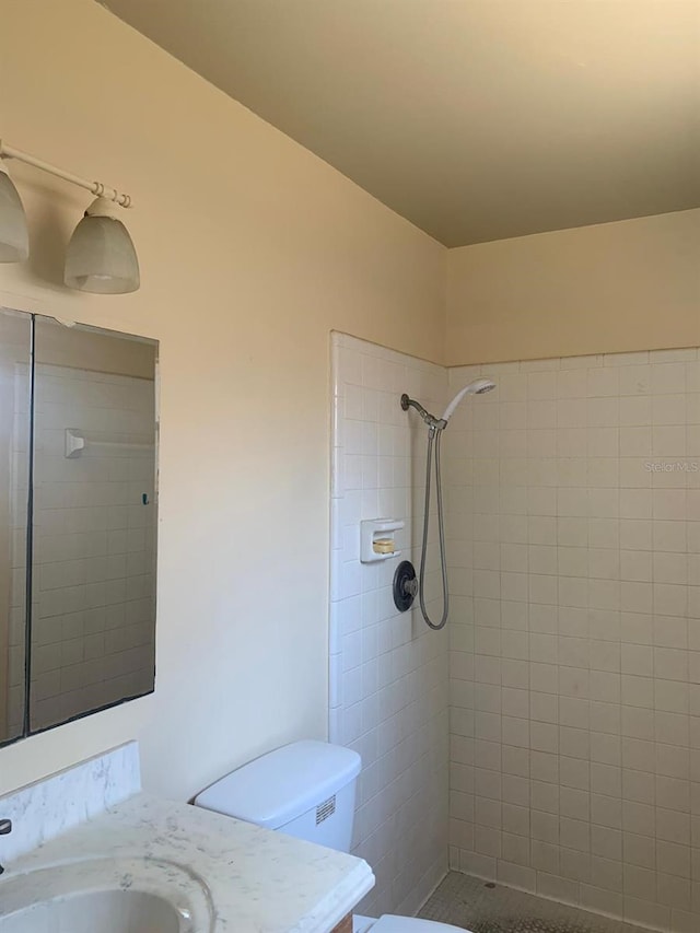 bathroom featuring a tile shower, vanity, and toilet