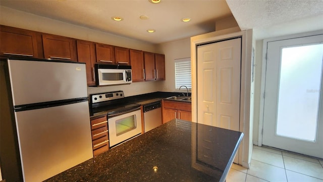 kitchen with dark stone countertops, appliances with stainless steel finishes, light tile patterned floors, and sink