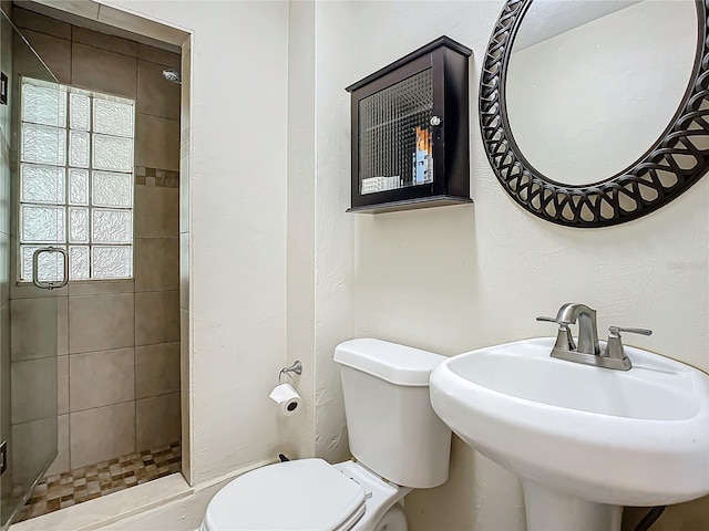 bathroom with tiled shower, sink, and toilet