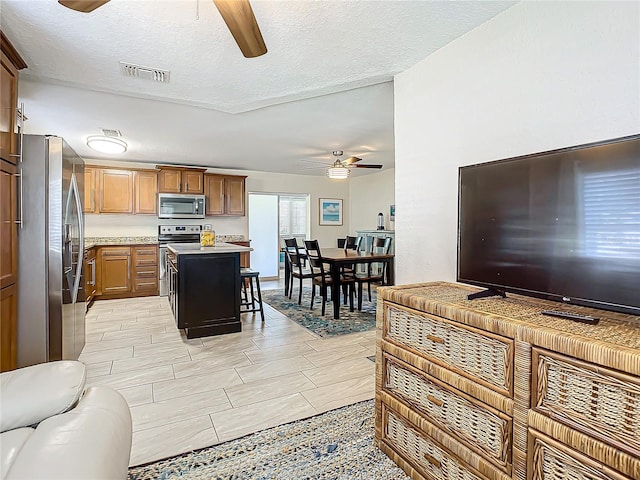 kitchen featuring stainless steel appliances, a textured ceiling, a breakfast bar area, ceiling fan, and a center island