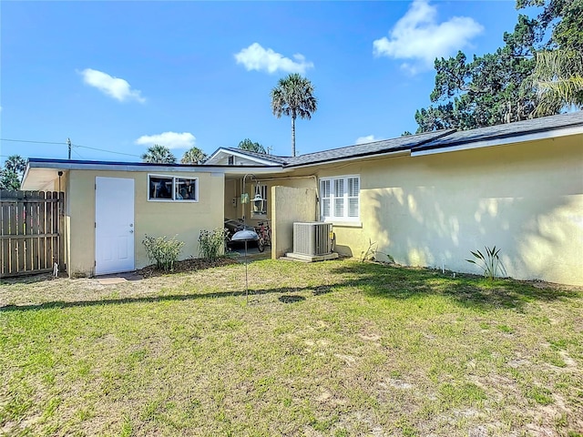 rear view of property with central air condition unit and a lawn