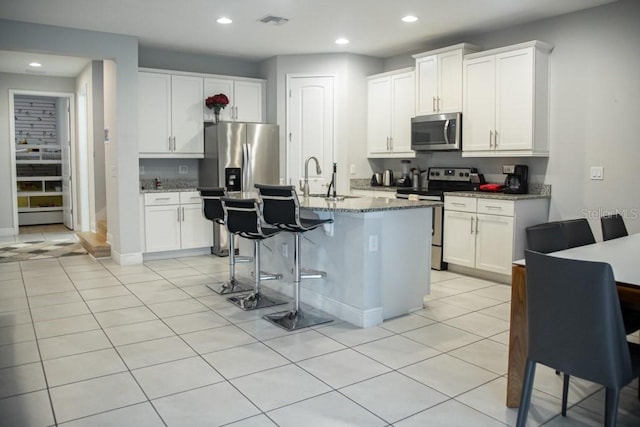 kitchen with dark stone counters, white cabinets, a kitchen island with sink, and appliances with stainless steel finishes