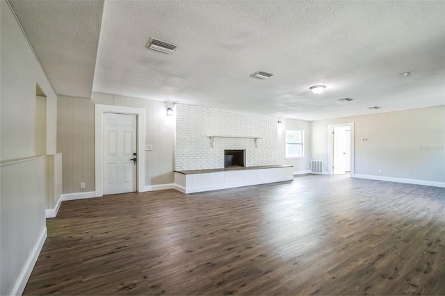 unfurnished living room with a textured ceiling, dark wood-type flooring, and a brick fireplace