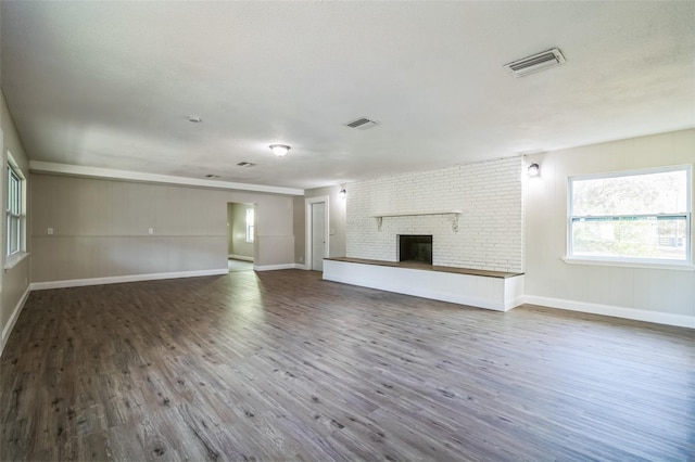 unfurnished living room with hardwood / wood-style flooring, a textured ceiling, and a brick fireplace