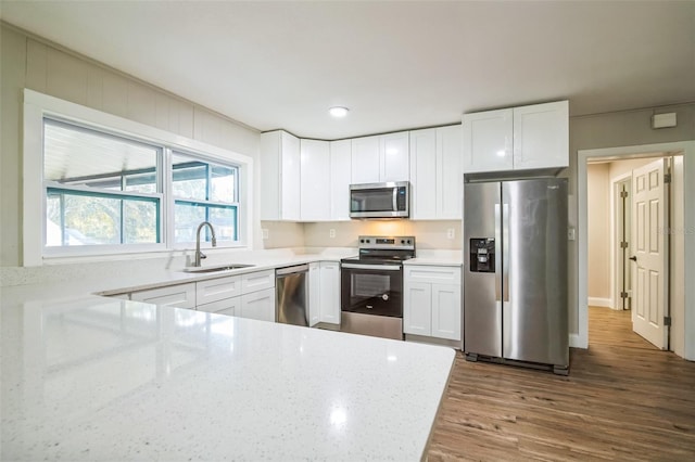 kitchen with appliances with stainless steel finishes, light stone counters, sink, wood-type flooring, and white cabinets