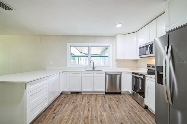 kitchen with appliances with stainless steel finishes, light hardwood / wood-style floors, white cabinetry, and sink