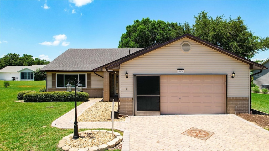 ranch-style home with decorative driveway, brick siding, a shingled roof, a front yard, and a garage