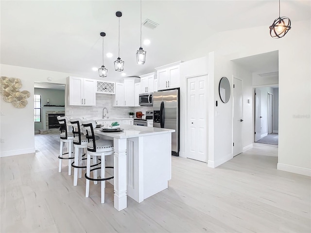 kitchen with white cabinetry, a kitchen island, appliances with stainless steel finishes, and decorative light fixtures