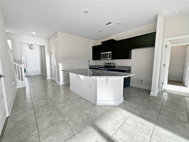 kitchen featuring stainless steel appliances, sink, dark stone countertops, an island with sink, and light tile patterned flooring