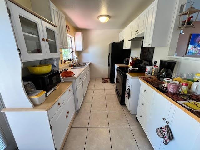 kitchen with white cabinets, light tile patterned flooring, electric range, and sink