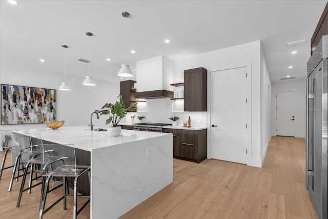 kitchen with light hardwood / wood-style floors, a large island with sink, dark brown cabinetry, hanging light fixtures, and a breakfast bar