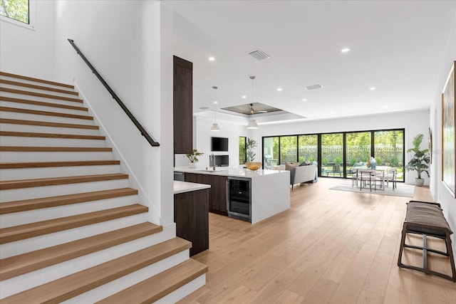 staircase with a wealth of natural light, wine cooler, sink, and light hardwood / wood-style flooring