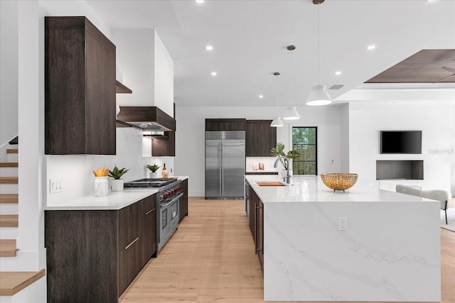 kitchen featuring a center island with sink, light hardwood / wood-style flooring, decorative light fixtures, high end appliances, and sink