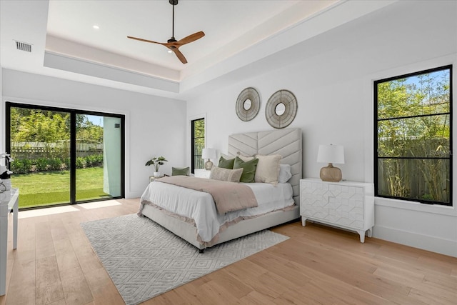 bedroom featuring light hardwood / wood-style flooring, access to outside, a tray ceiling, a high ceiling, and ceiling fan