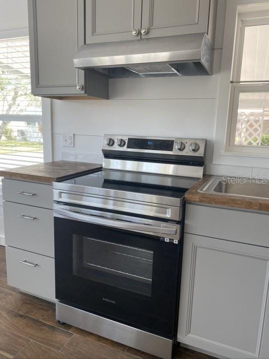 kitchen featuring gray cabinetry, butcher block counters, dark wood-type flooring, and stainless steel electric range