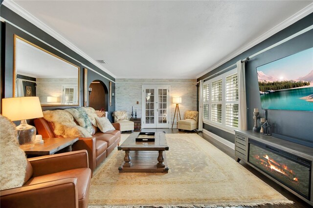 living room featuring visible vents, ornamental molding, a glass covered fireplace, french doors, and arched walkways