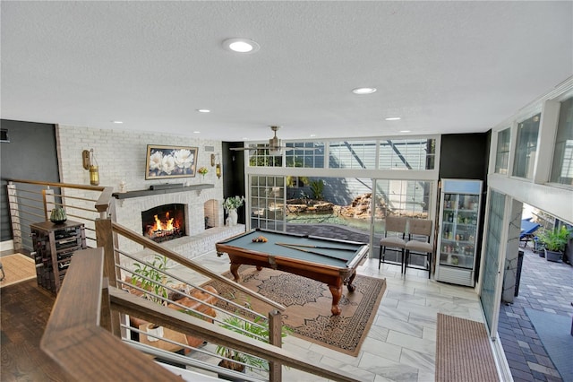 living room with floor to ceiling windows, a brick fireplace, a textured ceiling, and billiards