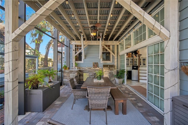 view of patio featuring outdoor dining space, glass enclosure, a ceiling fan, and an outdoor kitchen