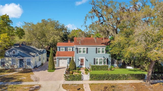 view of front facade with a front lawn, decorative driveway, a garage, and a chimney