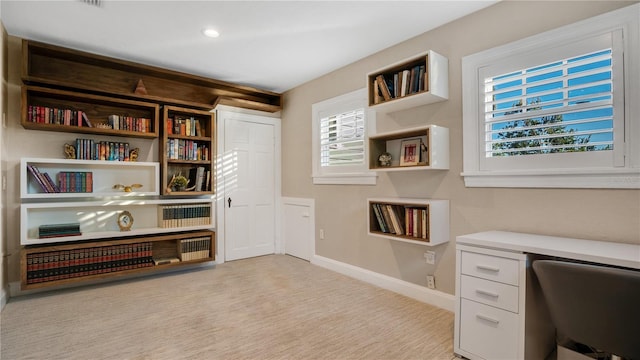 office area featuring baseboards, built in desk, and light carpet