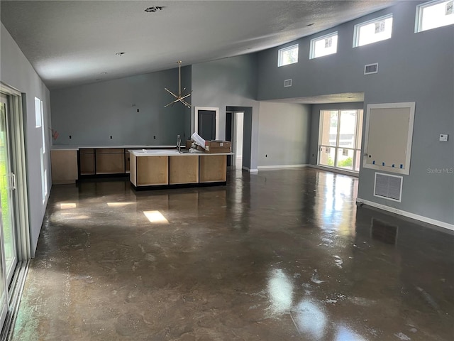 kitchen with a chandelier, a textured ceiling, a center island with sink, and high vaulted ceiling