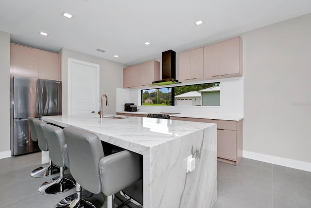 kitchen featuring light stone counters, a center island with sink, sink, and light brown cabinets