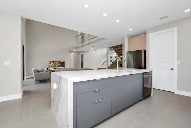 kitchen featuring a center island with sink, light stone counters, gray cabinetry, sink, and appliances with stainless steel finishes