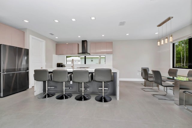 kitchen featuring pendant lighting, wall chimney exhaust hood, a breakfast bar, and stainless steel refrigerator