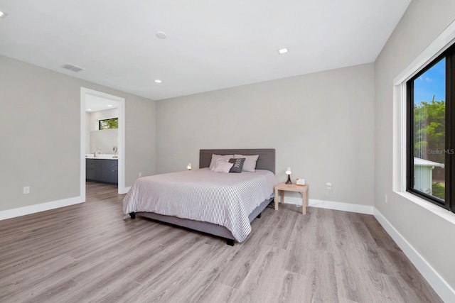 bedroom with ensuite bath, hardwood / wood-style flooring, and multiple windows