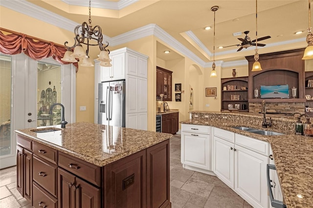 kitchen with white cabinetry, sink, stainless steel fridge, decorative light fixtures, and a center island with sink