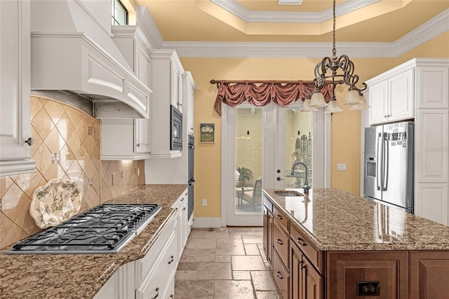 kitchen with appliances with stainless steel finishes, light stone counters, sink, white cabinets, and an island with sink