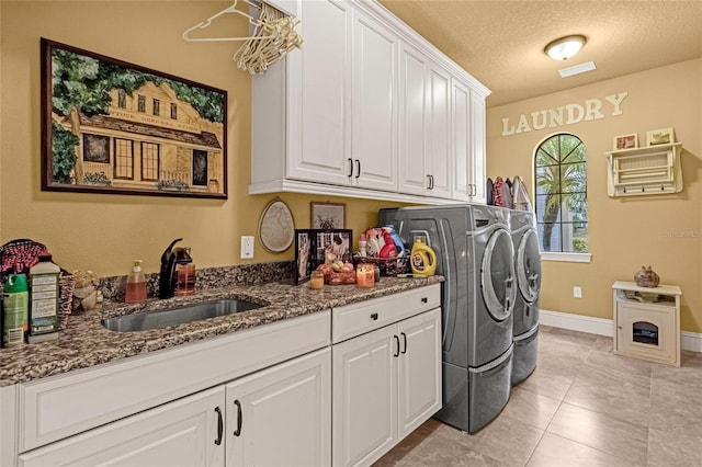 laundry area with cabinets, sink, light tile patterned floors, a textured ceiling, and washing machine and clothes dryer