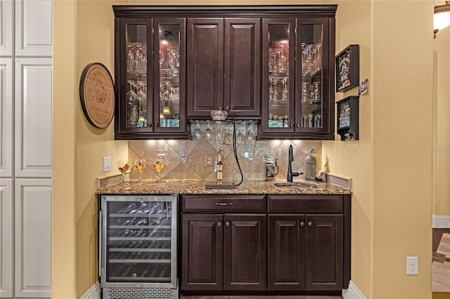 bar featuring sink, wine cooler, light stone countertops, tasteful backsplash, and dark brown cabinets