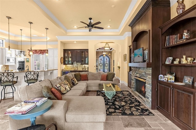 living room with a fireplace, a raised ceiling, ceiling fan, and crown molding