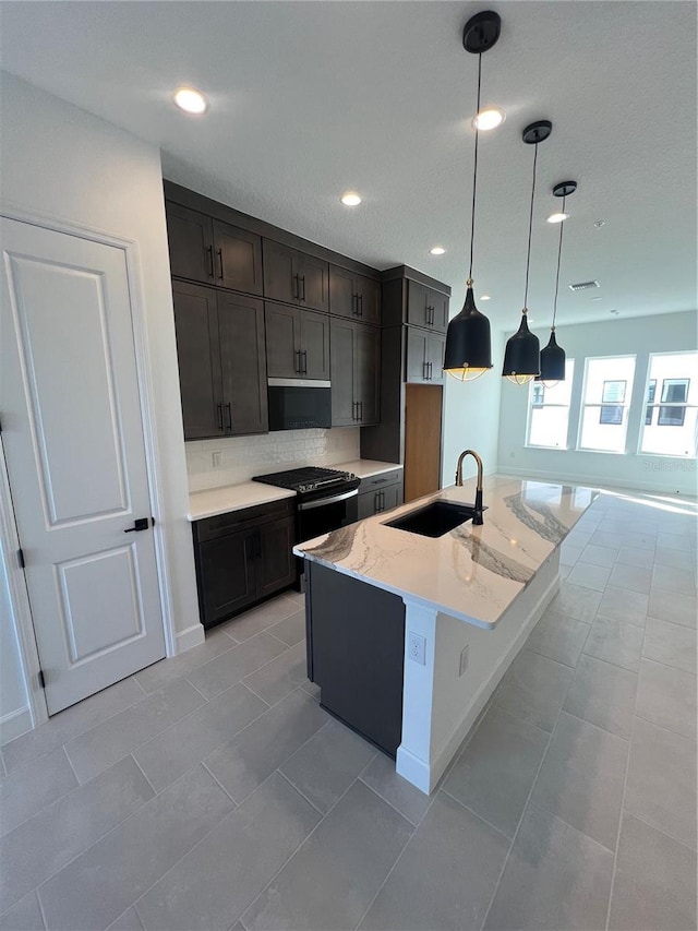 kitchen featuring decorative light fixtures, an island with sink, sink, backsplash, and black range with gas cooktop