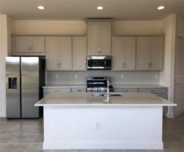 kitchen featuring stainless steel appliances, a center island with sink, backsplash, and gray cabinets