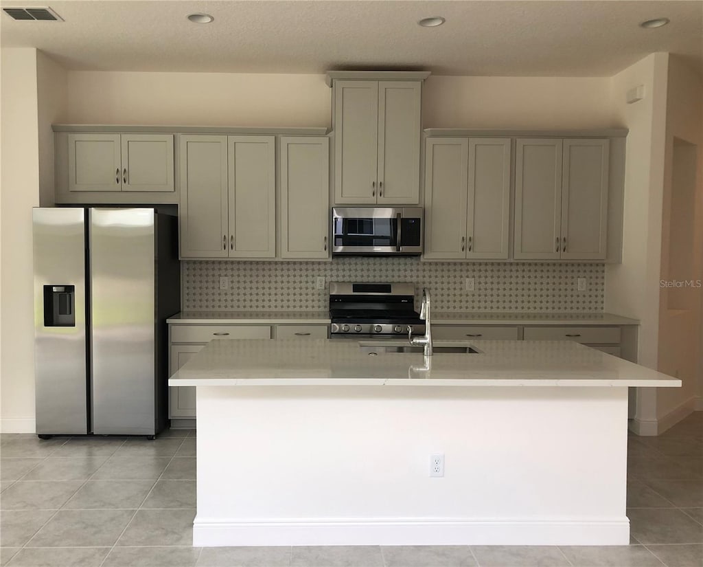 kitchen featuring gray cabinetry, a center island with sink, sink, and appliances with stainless steel finishes