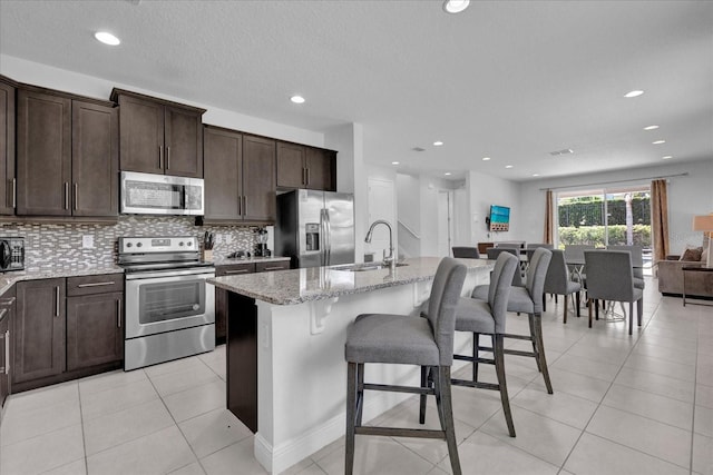 kitchen with stainless steel appliances, light stone counters, a kitchen island with sink, and sink