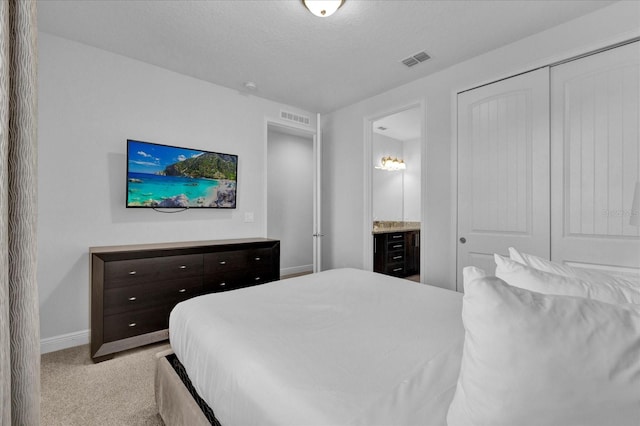 bedroom featuring ensuite bathroom, light colored carpet, a textured ceiling, and a closet