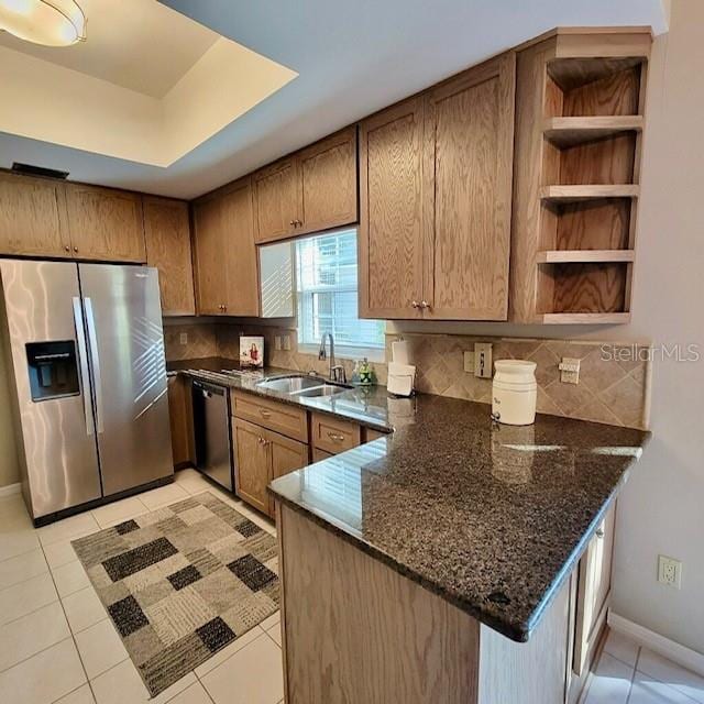 kitchen featuring sink, backsplash, kitchen peninsula, dark stone countertops, and appliances with stainless steel finishes