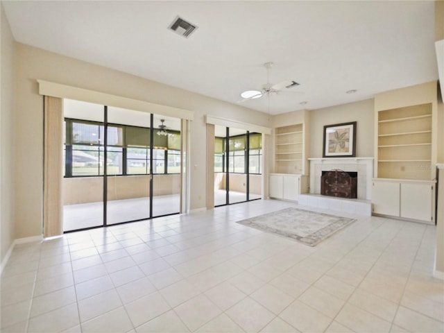 unfurnished living room with ceiling fan, a healthy amount of sunlight, built in features, and a tiled fireplace