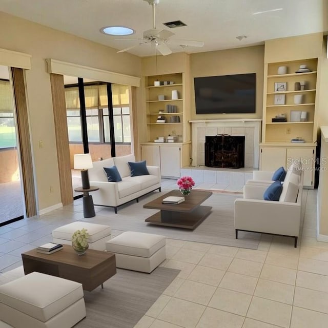 living room featuring built in shelves, ceiling fan, a fireplace, and light tile patterned floors