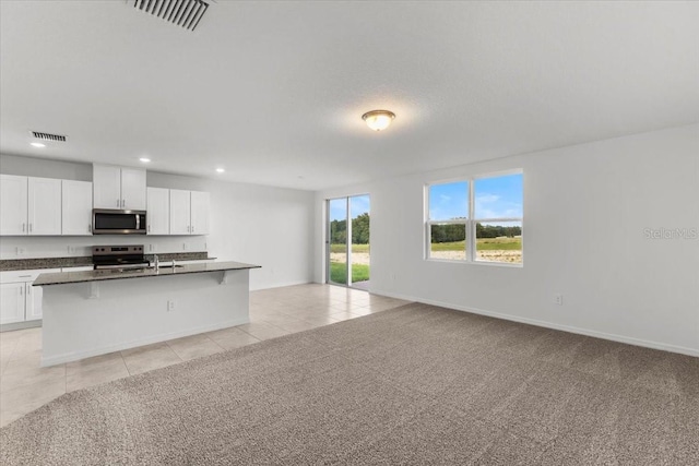 kitchen with appliances with stainless steel finishes, white cabinetry, a kitchen island with sink, and light carpet