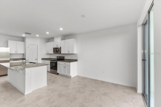 kitchen with an island with sink, stone countertops, a kitchen breakfast bar, stainless steel appliances, and white cabinets