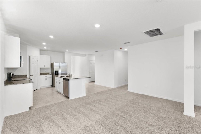 kitchen with light carpet, white cabinets, appliances with stainless steel finishes, and an island with sink